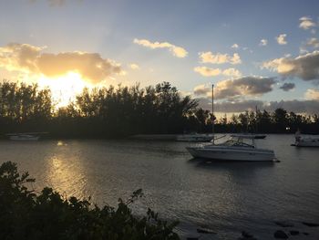 Boats moored in river against sky at sunset