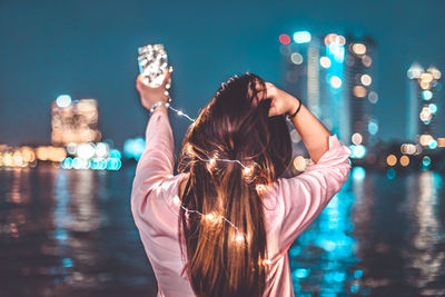 Woman standing by river in illuminated city at night