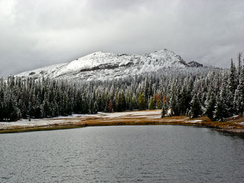 Scenic view of lake by snowcapped mountains against cloudy sky