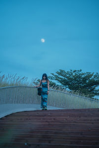 Rear view of woman walking on footpath against clear sky