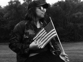 Young woman holding american flag while sitting at park