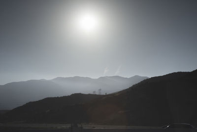 Sun shining over cars on road by mountains