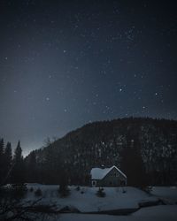 House on snowcapped mountain against sky at night