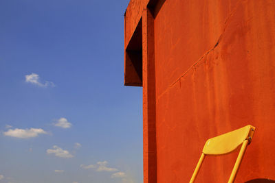 Low angle view of chair against orange wall and sky