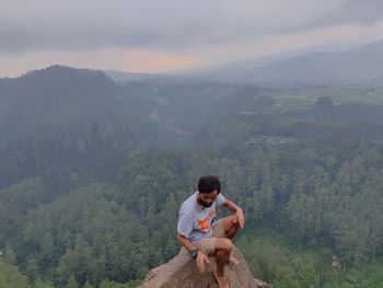 Young man sitting on mountain against mountains