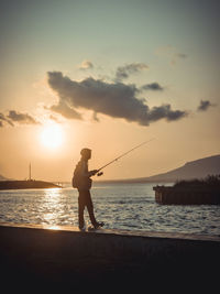 Silhouette man standing at beach against sky during sunset