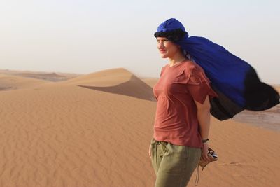 Smiling young woman wearing headscarf while standing on sand dunes at desert