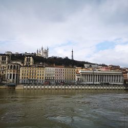 Buildings at waterfront against cloudy sky