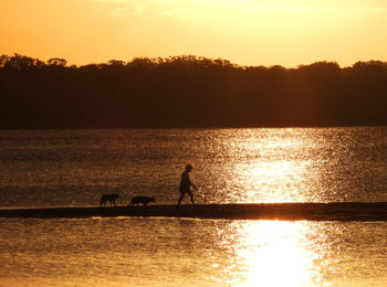 Silhouette people on sea against sky during sunset