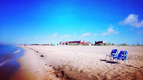 Deck chairs on beach against blue sky