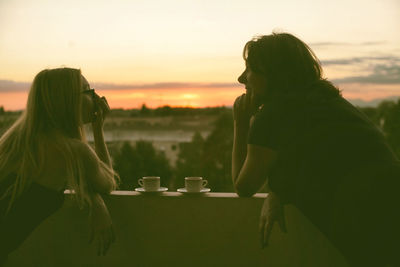 Mother and daughter talking against sky during sunset