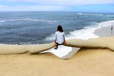 Rear view of woman sitting against sea at beach