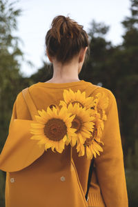 Rear view of woman standing on yellow flowering plant