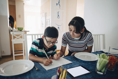 Teenage girl assisting brother in homework at dining table