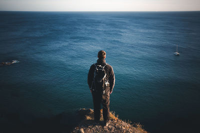 Rear view of backpacker looking at sea while standing on cliff