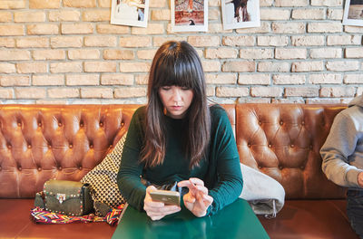 Young woman using phone while sitting on wall