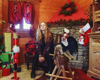 Full length portrait of woman sitting on chair at home during christmas 