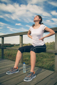Full length of young woman looking at railing against sky