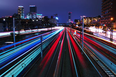 Light trails on railroad tracks amidst buildings in city at night