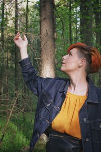 Mid adult woman standing by tree trunk in forest