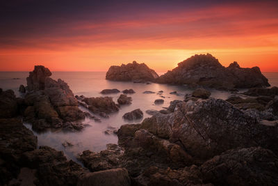 Rocks in sea against sky during sunset