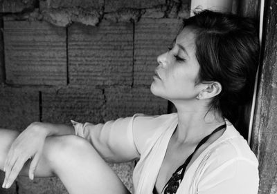 Side view of young woman sitting on window