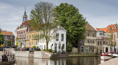 Canal by buildings and tree in city against sky