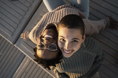 Smiling friends leaning on each other shoulder while sitting on bench