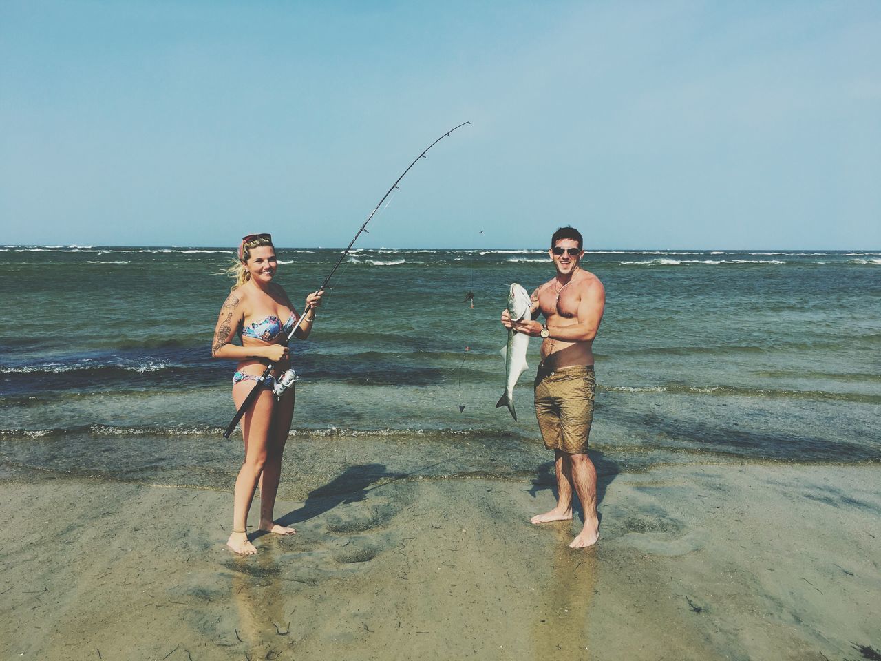 shirtless, two people, sea, standing, leisure activity, vacations, fishing, real people, holding, front view, full length, beach, nature, outdoors, smiling, boys, horizon over water, happiness, young men, day, weekend activities, looking at camera, young adult, water, sky, clear sky, togetherness, young women, men, adult, people