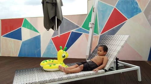 Full length of shirtless boy lying with inflatable ring on lounge chair