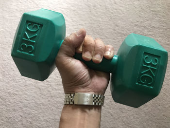 Cropped hand of man lifting dumbbell against wall