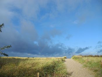 Road passing through field against cloudy sky