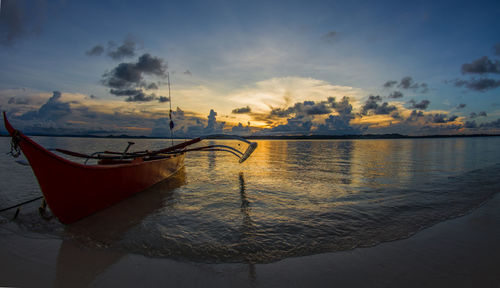 Outrigger canoe moored at beach against sky during sunset