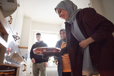 Woman taking food for eid al-fitr out of oven while cooking with family