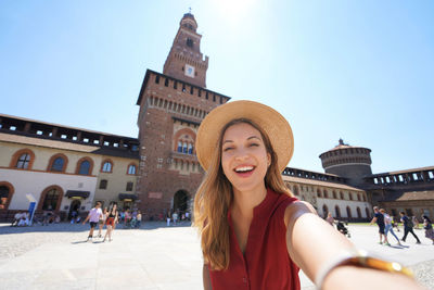 Attractive traveler girl taking self portrait of with sforza castle in milan, italy