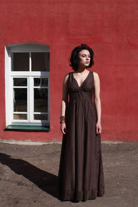 Beautiful woman in brown dress standing against red wall