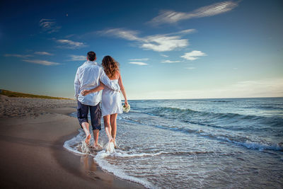 Rear view of couple walking on beach against sky