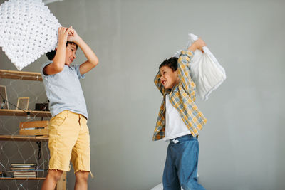 Brothers fighting with pillow while standing against wall