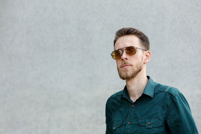 Portrait of young man wearing sunglasses while standing against wall