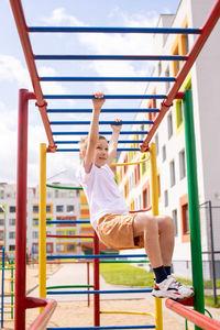 The boy does sports on horizontal bars of different colors