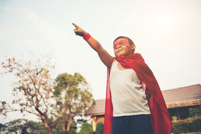 Low angle view of boy wearing cape while pointing against sky