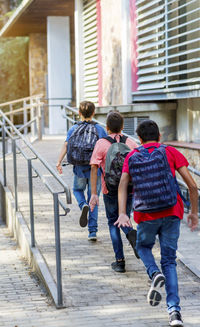 Rear view of friends with backpacks running on walkway