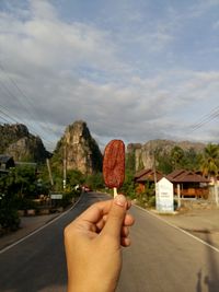 Midsection of person holding ice cream against sky