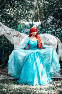 Smiling woman wearing crown with red hair sitting by sculpture