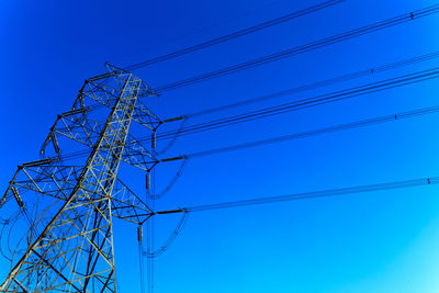 Low angle view of electricity pylon against clear blue sky