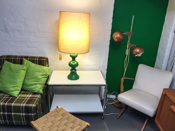 Illuminated lamp on table amidst sofa and chair on floor at home