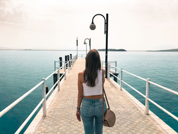 Rear view of woman standing on pier over sea against sky