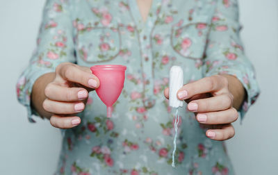 Midsection of woman holding cup and tampon