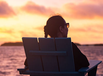 Side view of woman using laptop while sitting on beach against orange sky