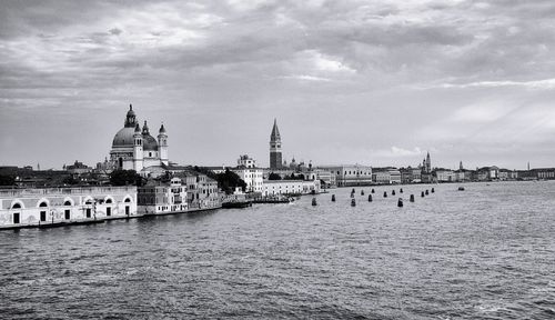 View of buildings by river against cloudy sky